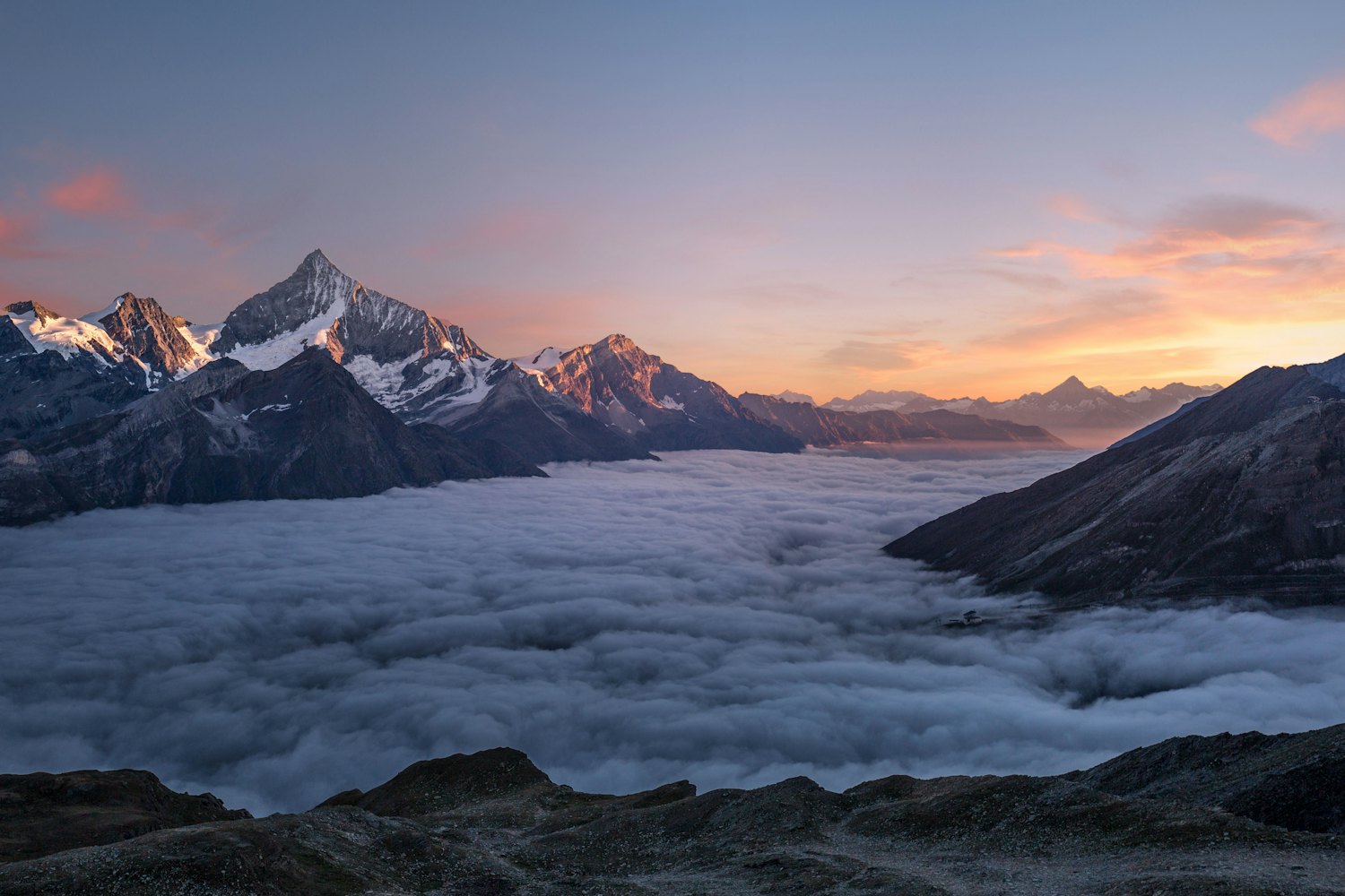 First light over a range of mountain peaks rising above a sea of cloud